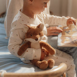 Child holding a plush fox toy and a book sitting on a bed