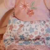 Close-up of the Little Dutch Hug Doll Rosa's embroidered floral T-shirt and blue and pink floral skirt with lace trim detail