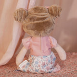 Back view of the Little Dutch Hug Doll Rosa sitting, showing brown fluffy bun hairstyle, pink T-shirt and floral skirt with Little Dutch label
