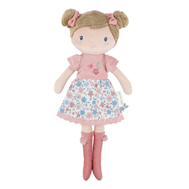 Little Dutch Hug Doll Rosa standing upright, with brown bun hairstyle, pink bows, embroidered floral T-shirt, floral skirt and pink pompom boots, on a white background