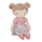 Little Dutch Hug Doll Rosa sitting, showing soft brown bun hair with pink bows, embroidered pink T-shirt and blue and pink floral skirt, on a white background
