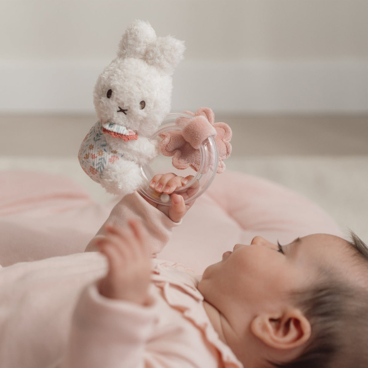 Baby holding a Miffy soft toy rattle with a blurred background