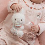 Child holding a white fluffy Miffy toy with a transparent ring with balls in, wearing a pink outfit.