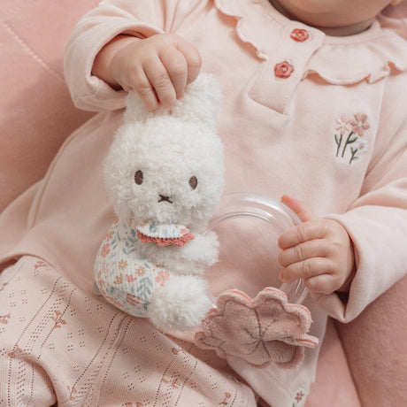 Child holding a white fluffy Miffy toy with a transparent ring with balls in, wearing a pink outfit.