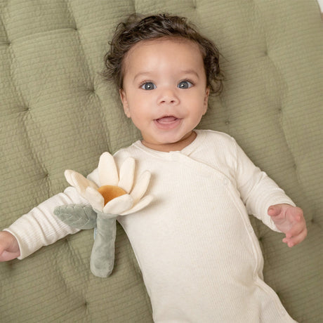 Baby lying on a green cushion holding a flower shaped soft toy