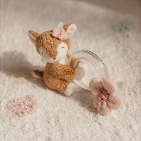 Stuffed fox toy with floral headband sitting next to a clear glass teacup on a soft surface.