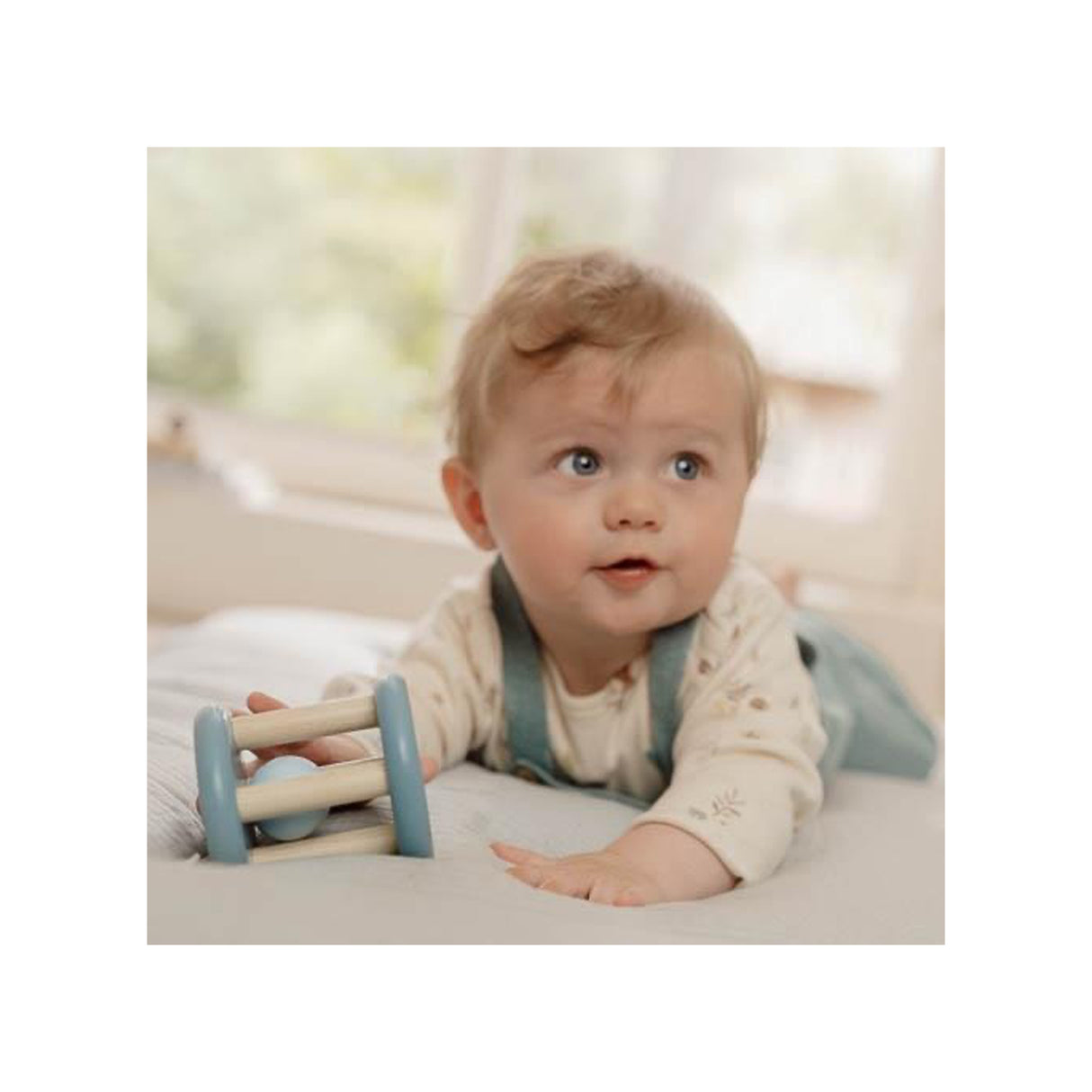 Baby playing with a Blue Wooden baby rattle toy with toadstool and leaf design on a soft surface