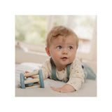 Baby playing with a Blue Wooden baby rattle toy with toadstool and leaf design on a soft surface