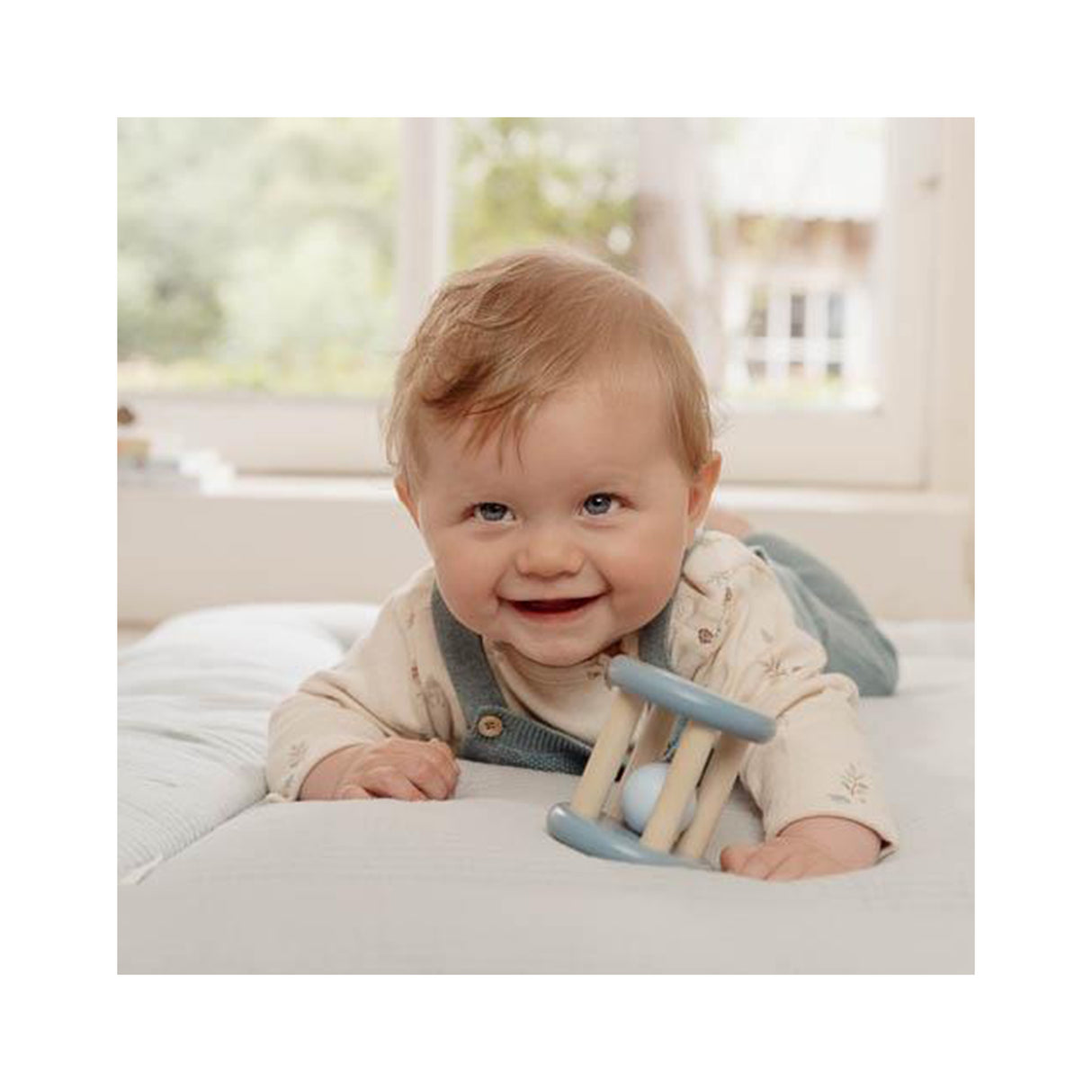 Baby lying on a bed holding a blue wooden rattle toy