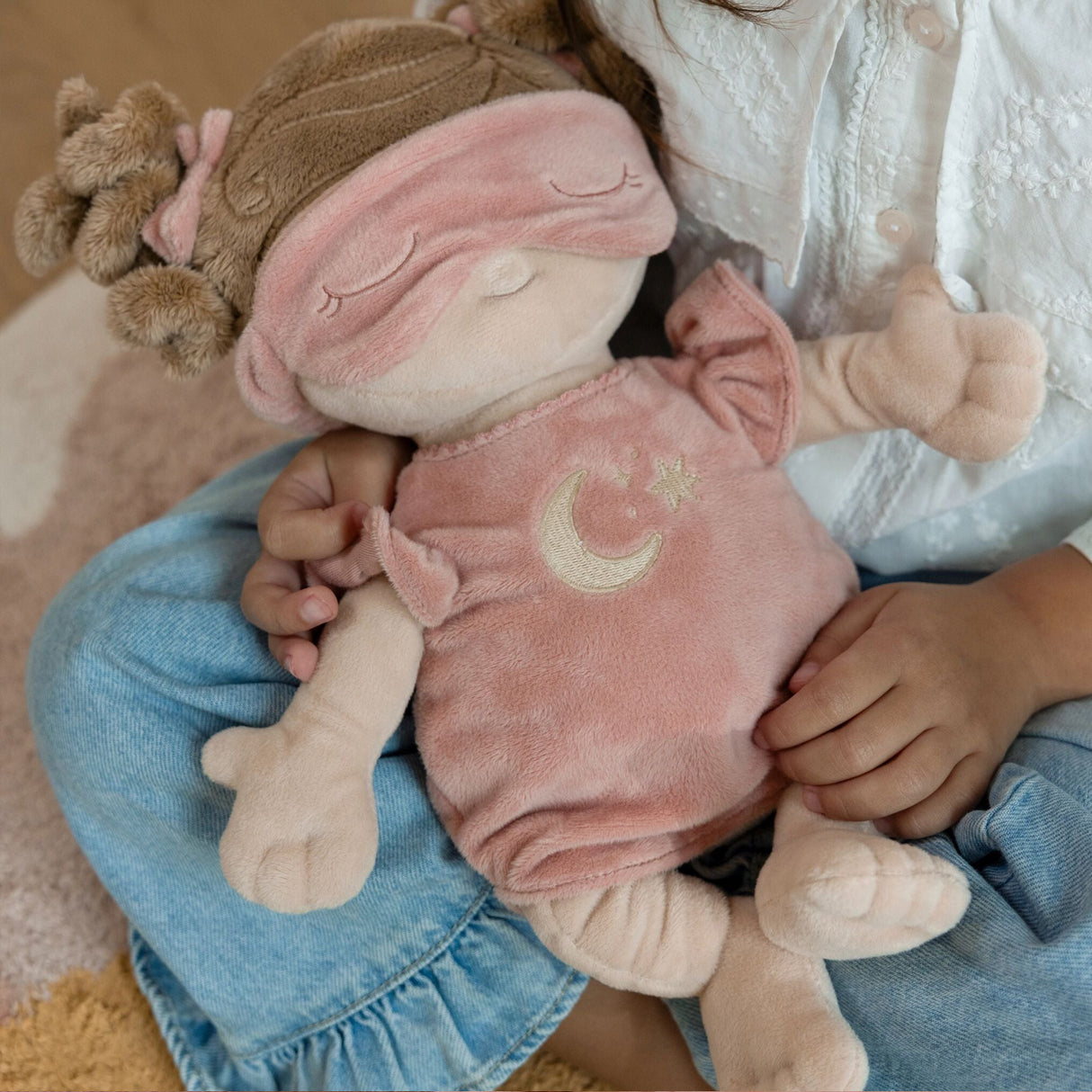 Child holding a baby doll with a moon and star design pink outfit, sitting on a carpeted floor.