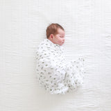 Newborn baby swaddled in a white blanket with bunny and leaf pattern on a textured white surface