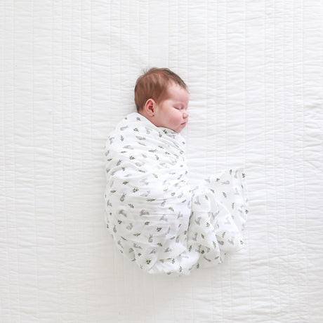 Newborn baby swaddled in a white blanket with bunny and leaf pattern on a textured white surface