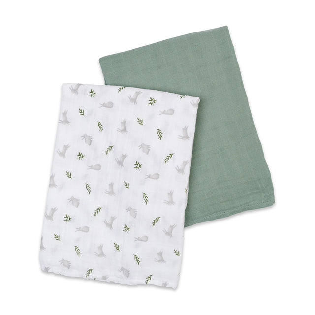 Two baby cotton swaddles, one white with a rabbit and leaf pattern and the other solid sage green, on a white background.