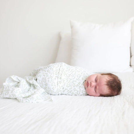 Newborn baby swaddled in a white leaf muslin on a white bed