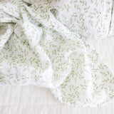 White cotton muslin baby swaddle with green leaf pattern on a white background