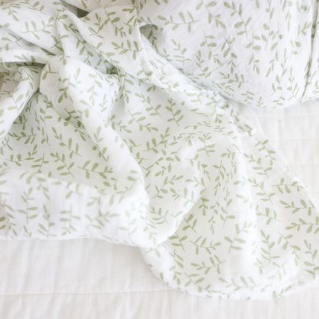 White cotton muslin baby swaddle with green leaf pattern on a white background