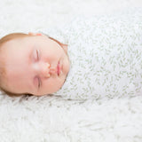 Newborn baby sleeping peacefully wrapped in a white leaf patterened swaddle.