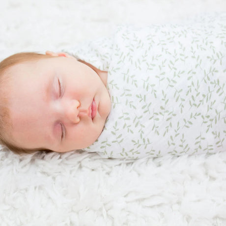 Newborn baby sleeping peacefully wrapped in a white leaf patterened swaddle.
