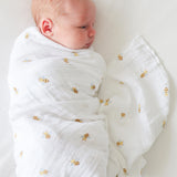 Newborn baby wrapped in a white swaddle with gold bee patterns on a light background