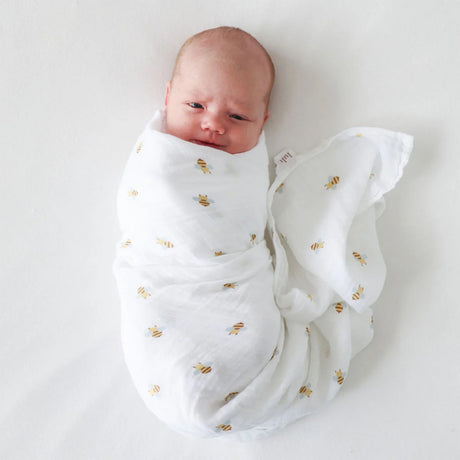 Newborn baby wrapped in a white swaddle with bee patterns on a white background