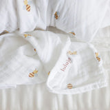 White baby swaddle with bee design and 'lulujo' branding lable on a light background