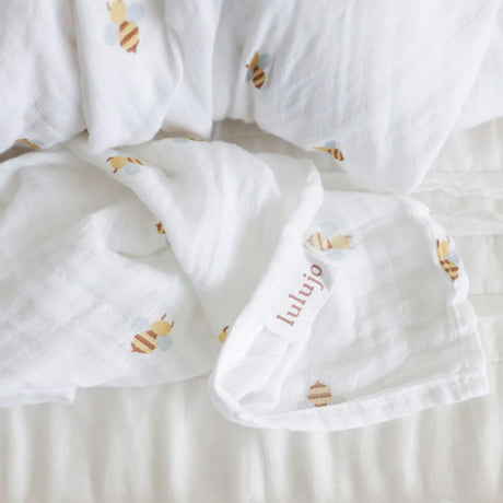 White baby swaddle with bee design and 'lulujo' branding lable on a light background