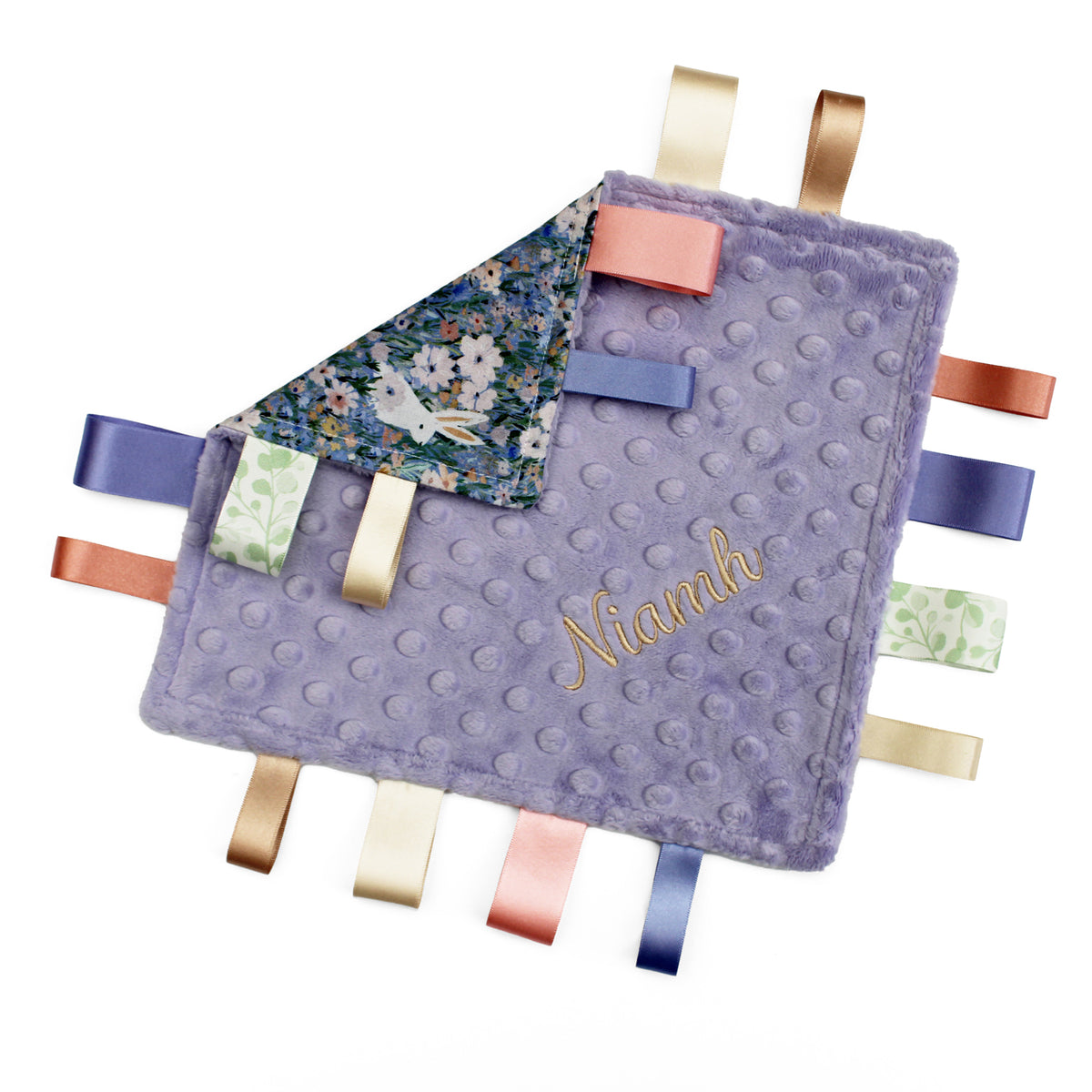 A lavender purple textured baby lovey blanket with a name embroidered in gold on the front. The back side features a small floral print with a white rabbit.