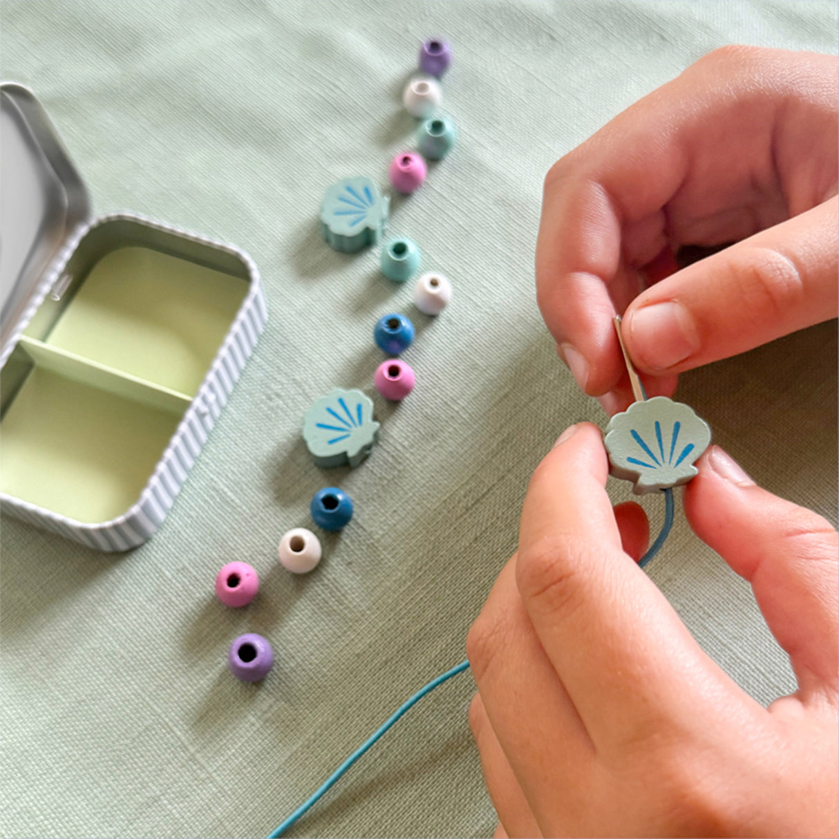 Person stringing colorful beads on a thread with a small container nearby.