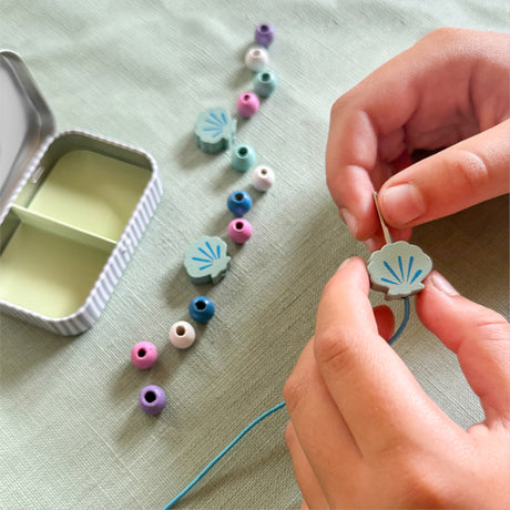 Person stringing colorful beads on a thread with a small container nearby.