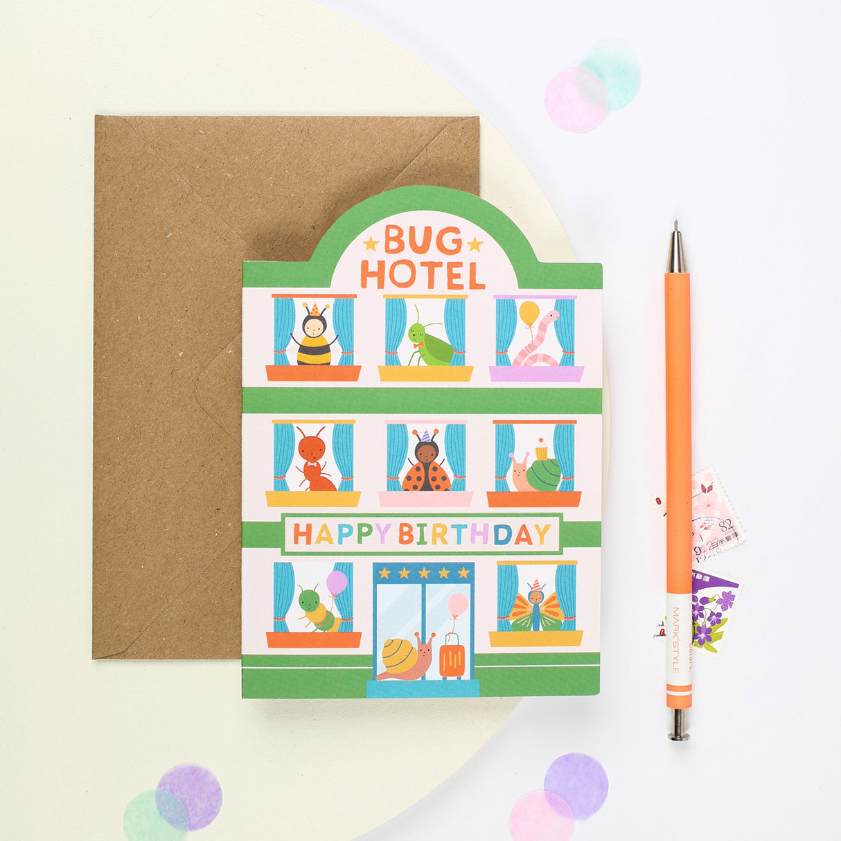 Birthday card with 'Bug Hotel' design on a white background. Insects at each window of the hotel and a snail with a suitcase at the door