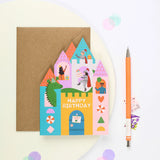 Mifkins Fairytale Castle birthday card with kraft envelope next to an orange pen, showing colourful castle design with dragon and fairytale characters