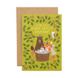 A green Birthday card with illustrated bear, fox, hedgehog, owl and rabbit around a cake on a tree stump,  with leaves surrounding them. Comes with a brown envelope.