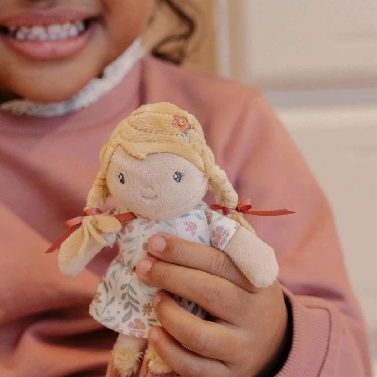 Child holding a small doll with blonde hair and a pink floral outfit.
