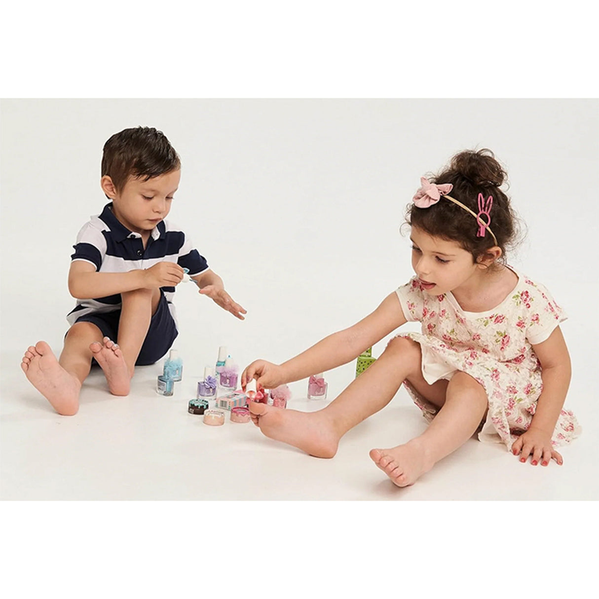Two children playing with nail polish on a white background