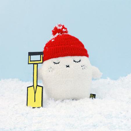 Cream monster with a red hat and yellow shovel in the snow against a light blue sky