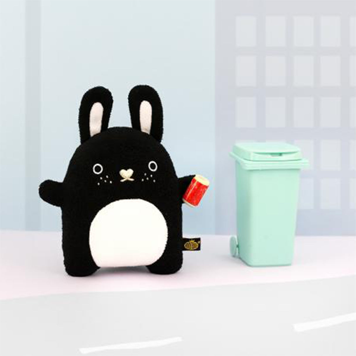 Black and white bunny soft toy standing next to green bin
