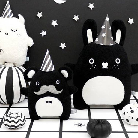 Black and white bunny soft toy with heart shaped nose standing next to other soft toys