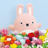 Soft pink toy rabbit surrounded by colourful flowers on a light blue background