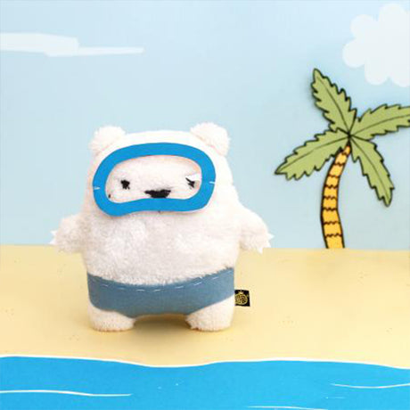 polar bear soft toy in swimming trunks and googles with a palm tree in the back