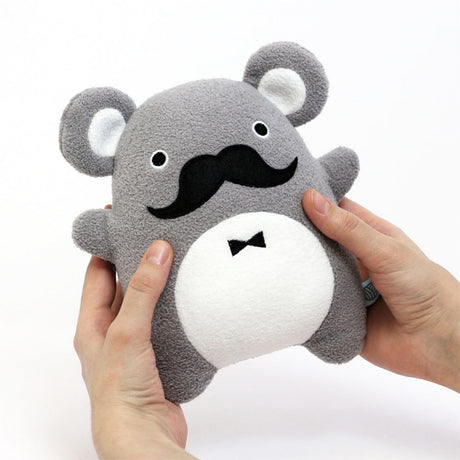 Gray plush toy with a mustache held by a hand on a white background