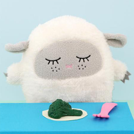 Plush toy sheep with a face eating broccoli on a blue background