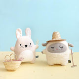 Two plush toys, a rabbit and a sheep, on a yellow surface with a light blue background.