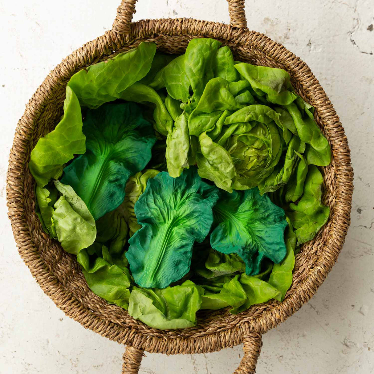 Wicker basket filled with green leafy vegetables and kale baby rubber teethers on a light background