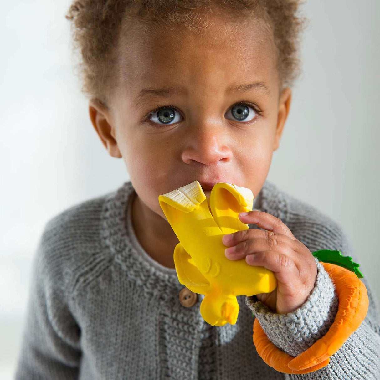 Child holding a yellow banana teething toy with a plain background