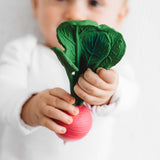 Baby holding a natural teether rattle in the shape of a pink raddish