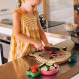 Young girl in a yellow dress cutting vegetables on a wooden cutting board and putting them on the raddish dish