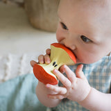 Baby holding and chewing on a red and yellow teething toy.