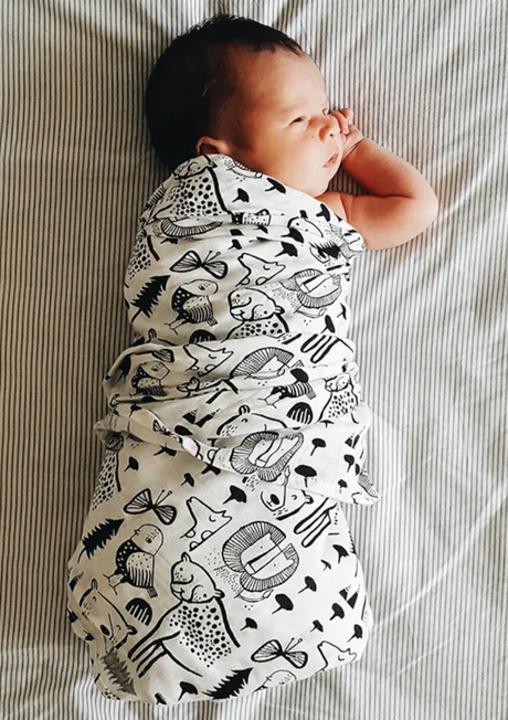 Baby with wild animal print swaddle lying on a light fabric