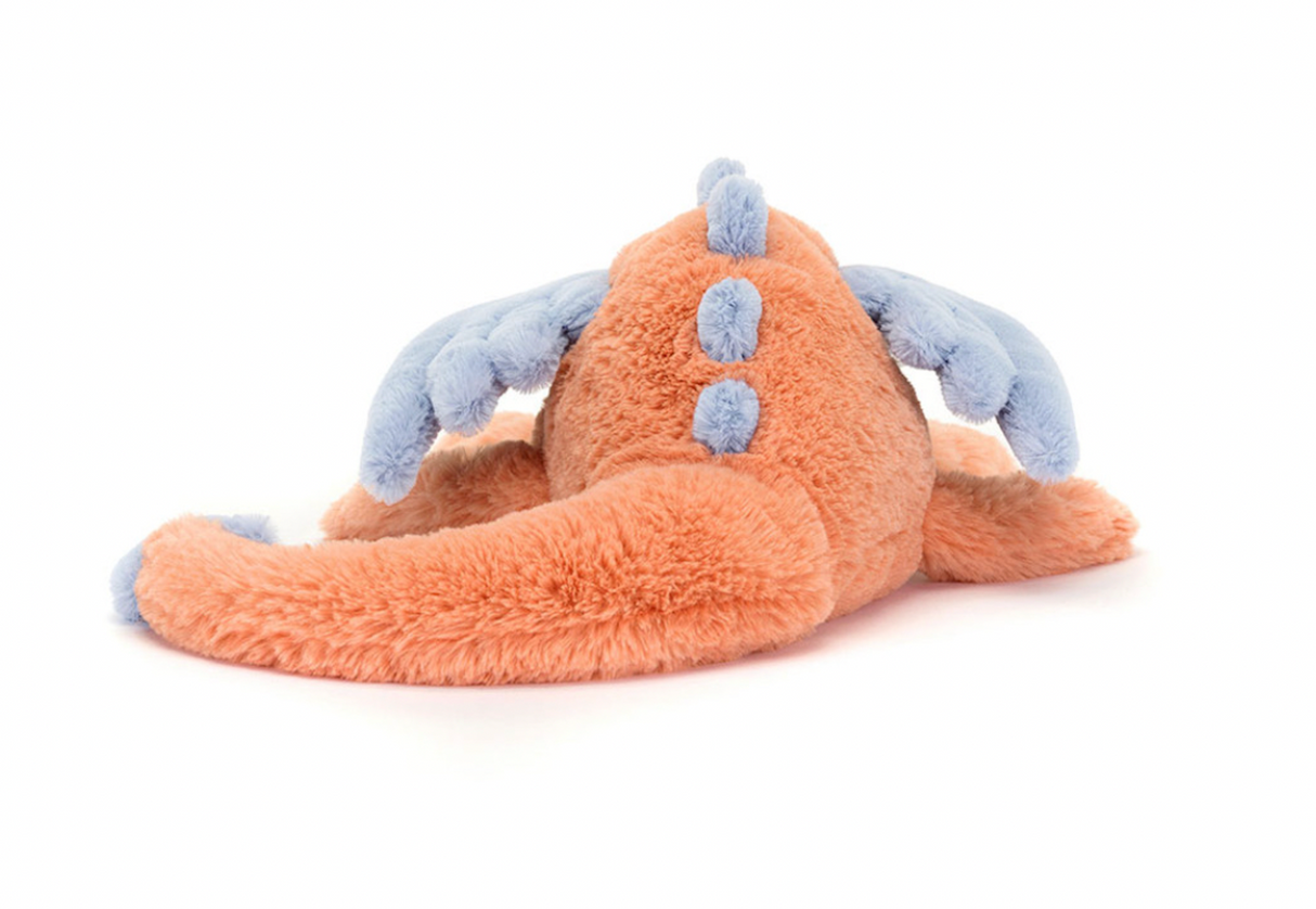 A plush toy representing a dragon with coral and blue colors, lying down with a content expression.