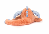 A plush toy representing a dragon with coral and blue colors, lying down with a content expression.